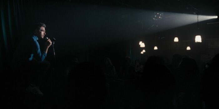 A spotlight illuminates a stage comedian in dark club in Ezra.