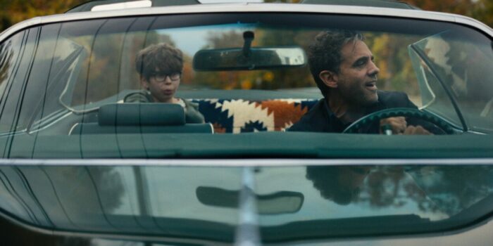 A boy sits in the backseat of a convertible while his father drives in Ezra.