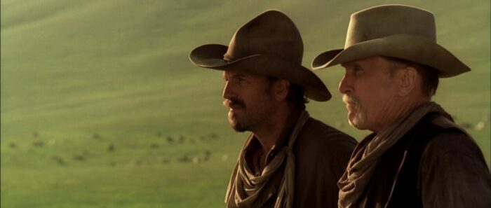 Two men on horseback look across ranch land in Open Range.
