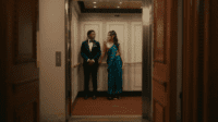 A man and woman in formal wear stand at the end of a hallway in Midas.