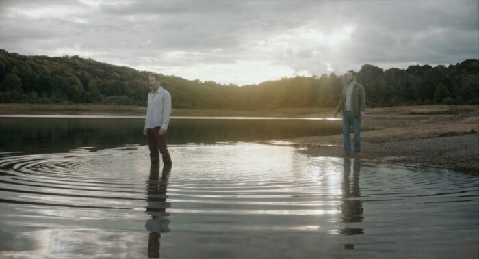 David Duchovny and Logan Marshall-Green as Marty and Ted in Reverse the Curse (2023). Courtesy of Vertical and R&CPMK. Marty wades out into a shallow pond as his estranged son stands on the shore calling to him.