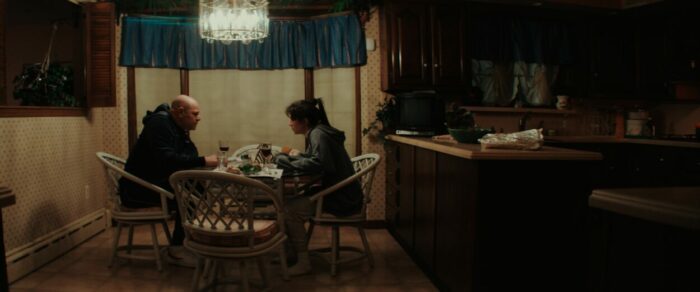 Domenick Lombardozzi and Emily Bader as Joe and Connie Larusso in Fresh Kills (2023). Courtesy of Quiver Distribution. Rose sitting a table with her father Joe in a darkened kitchen while she confronts him about his mob ties.
