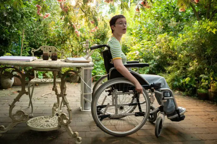 Lola Petticrew as Tuesday in Tuesday. Credit: By Kevin Baker. Courtesy of A24. Dying teenager Tuesday sits in a wheelchair in the backyard patio surrounded by lush greenery.