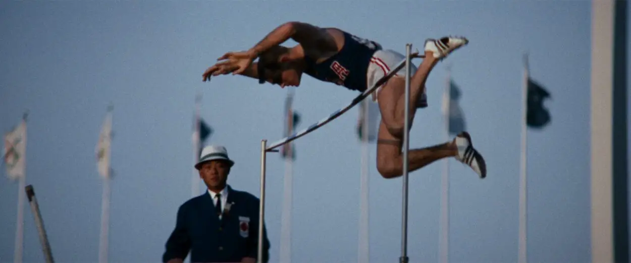 A an athlete vaults over a high-bar during the 1964 Tokyo Olympics as a judge looks on, as depicted in Tokyo Olympiad.