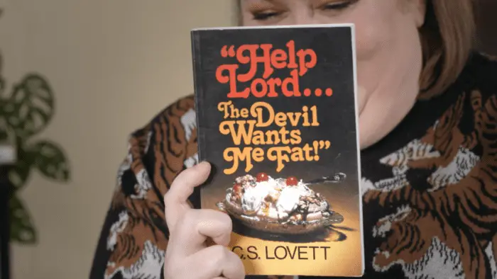 Aubrie Gordon holds a copy of a book titled "Help Lord... The Devil Wants Me Fat" by C. S. Lovett.