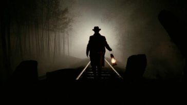 A man holding a lantern is backlit on train tracks in a western film.