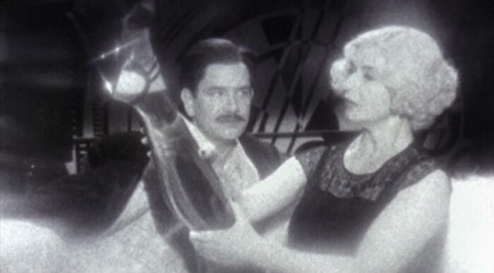 A man talks to a woman adjusting her tall boot in Guy Maddin's The Saddest Music in the World