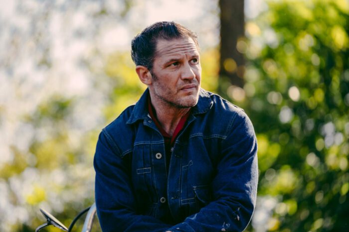 A man in a leather jacket looks across a park in The Bikeriders.