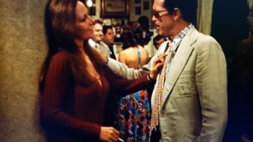 Isela Vega and Warren Oates as Elita and Bennie in Bring Me the Head of Alfredo Garcia (1974). Screenshot off MGM+. Elita and Bennie meeting in a fancy restaurant, her in a red dress eying him with love, while he stands in a shabby suit regarding her with disgust.