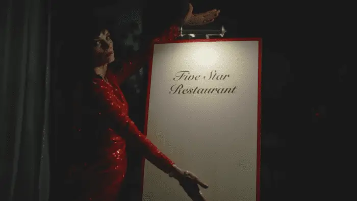 Lorraine Farris in CRUMB CATCHER. Courtesy of Doppelgänger Releasing. Rose in a red sequin dress displaying a sign that reads: five-star restaurant.