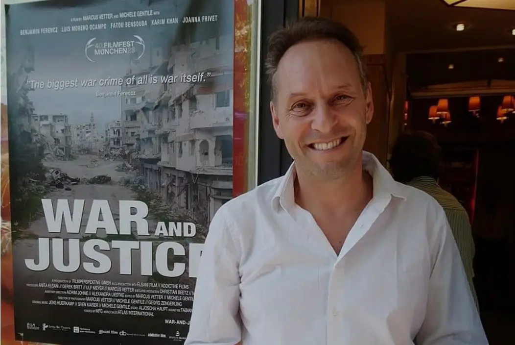 Marcus Vetter smiles in front of a poster for War and Justice.