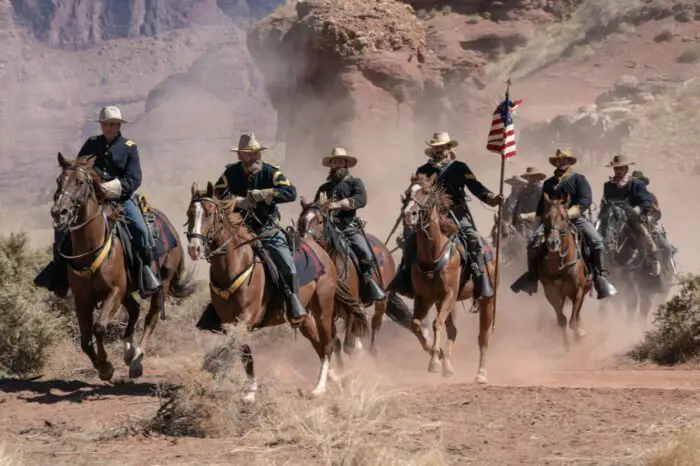 A calvary of soldiers ride quickly on horseback kicking up dust in Horizon: An American Saga.