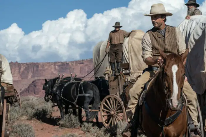 A man leads a train of covered wagons in Horizon: An American Saga.