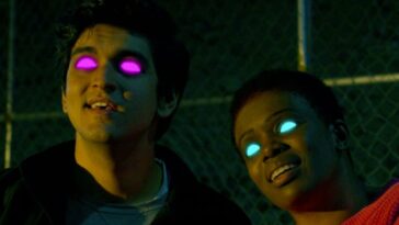 Two united aliens--one w young white man with black hair and pink glowing eyes, the other a black woman with short hair and blue glowing eyes--smile.