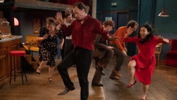 A slender middle aged man leads a dance in a small bar.