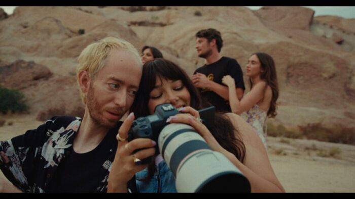 A female photographer helps a man see through her camera's viewfinder.