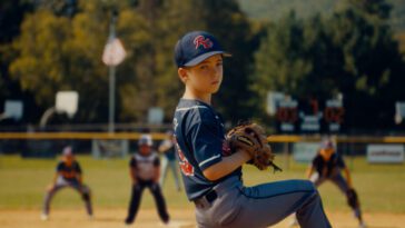 A young baseball player winds up for a pitch in Rally Caps.