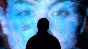 A silhouetted figure stares at a face of a woman displayed onscreen.